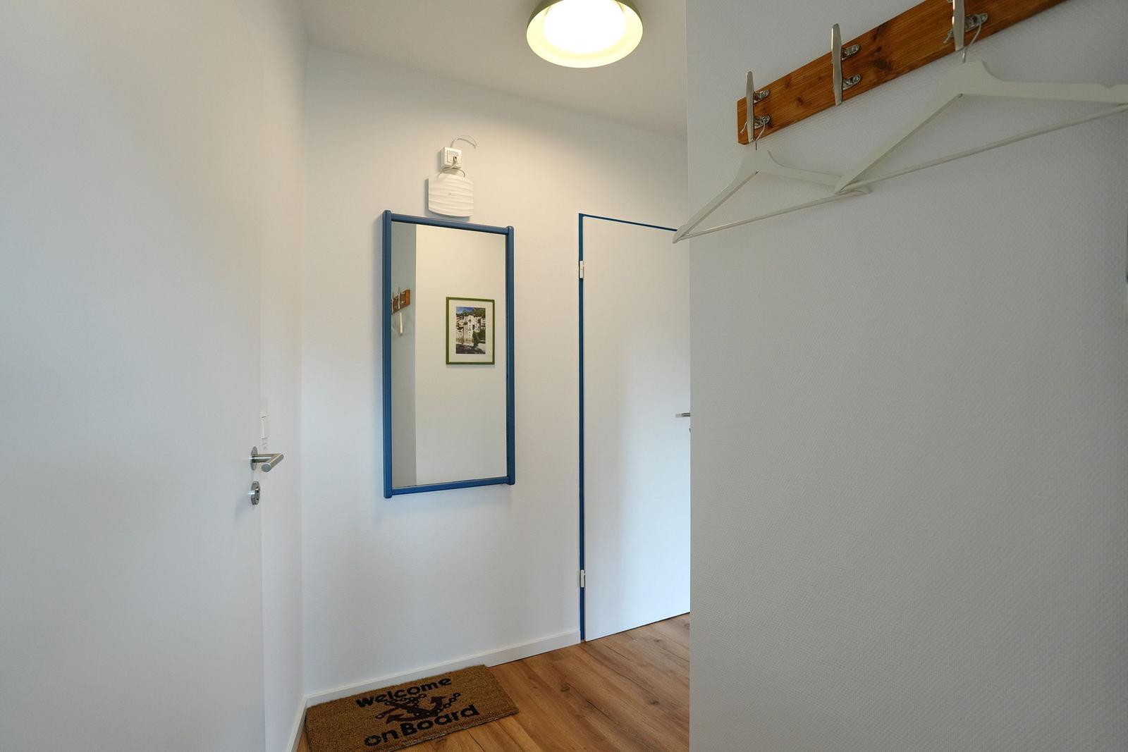 Eingangsbereich mit Spiegel, Holzboden und Kleiderhaken an der Wand.