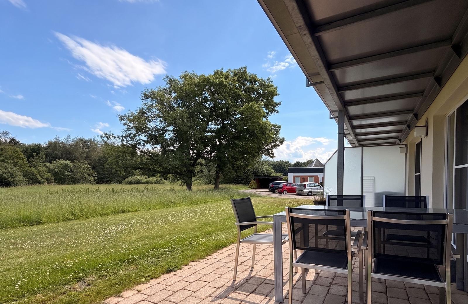 Terrasse mit Tisch und Stühlen. Blick auf grünes Feld und Baum.