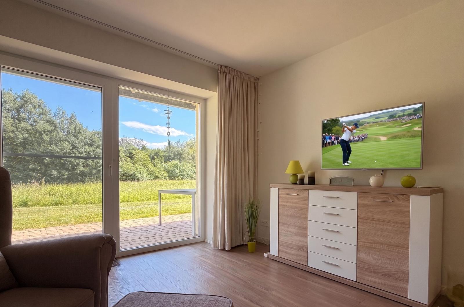 Wohnzimmer mit TV, Schiebetür und Blick auf Grünfläche