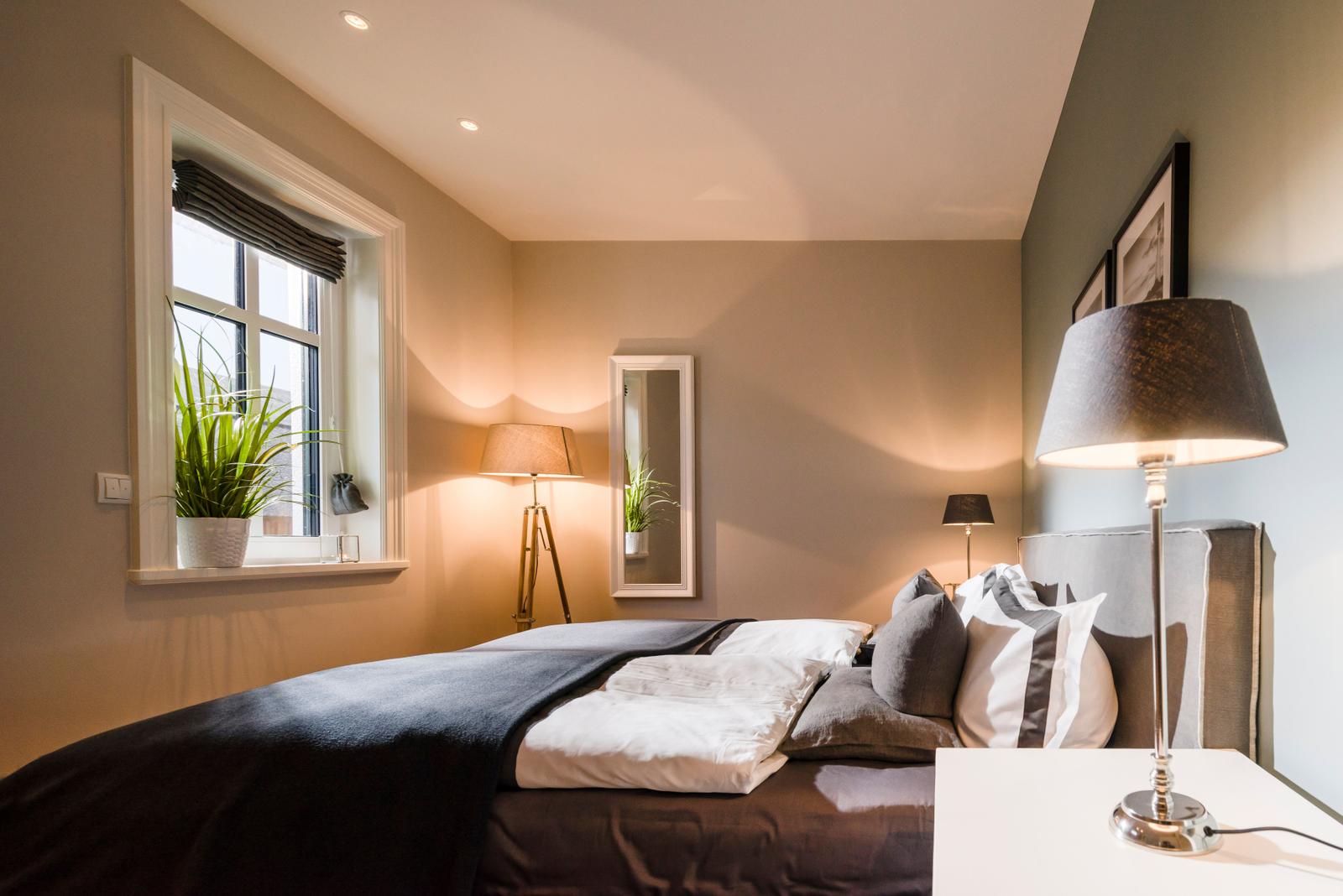 Schlafzimmer mit Bett, Nachttisch, Stehlampe und Fenster mit Pflanze.