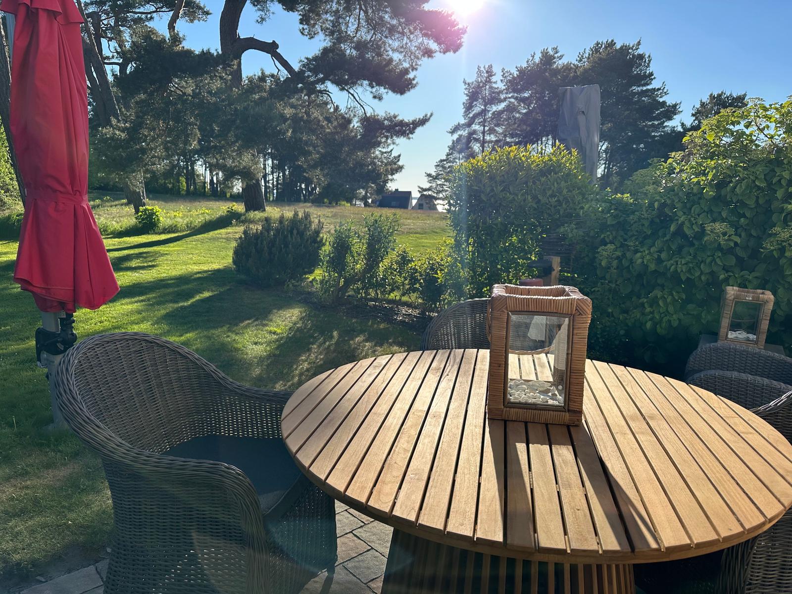 Runder Holztisch mit Stühlen und rotem Sonnenschirm im Garten.