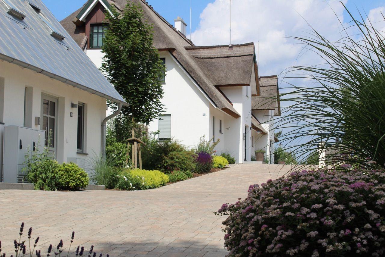 Haus mit strohgedecktem Dach und gepflastertem Weg durch Garten mit Blumen.