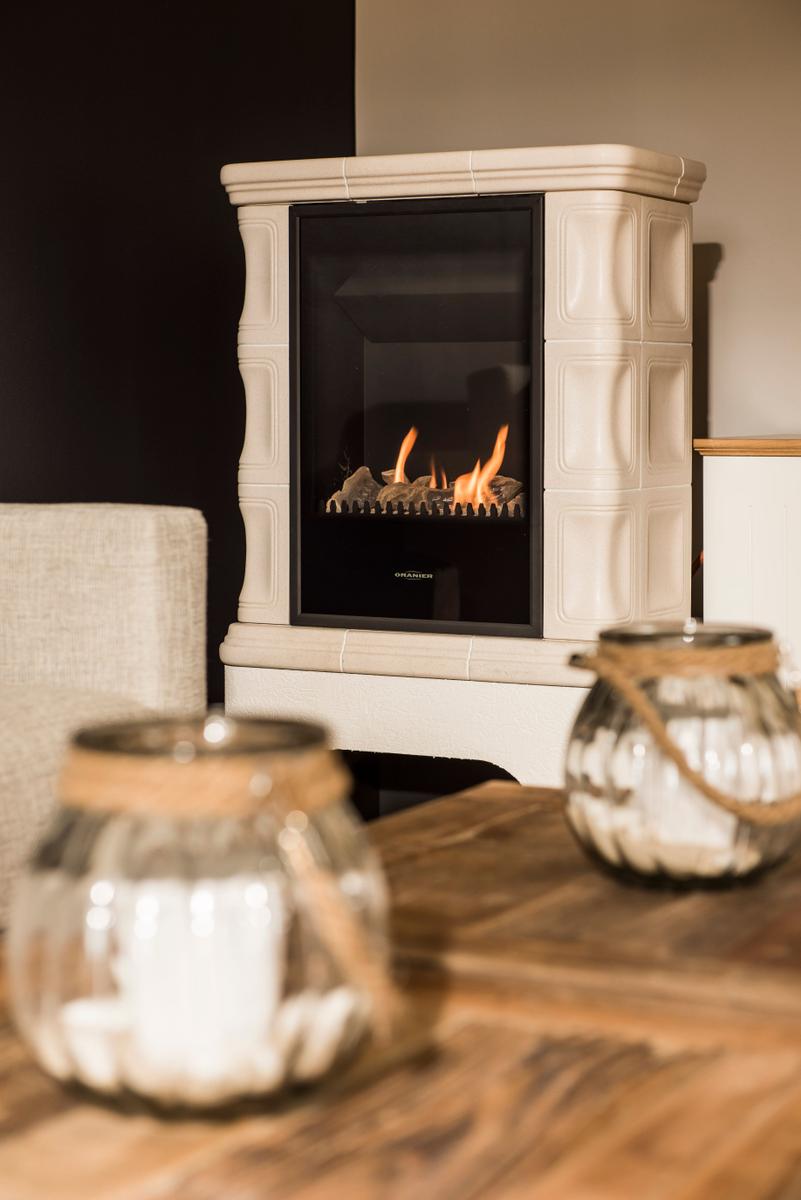 Ein Kamin mit brennendem Feuer steht im Raum. Vor ihm befindet sich ein Holztisch mit zwei Glasbehältern.