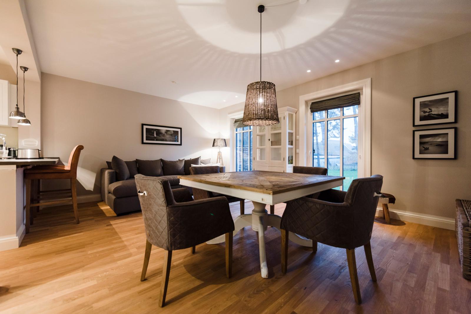 Essbereich mit Tisch, Stühlen und Sofa. Holzboden und große Fenster.