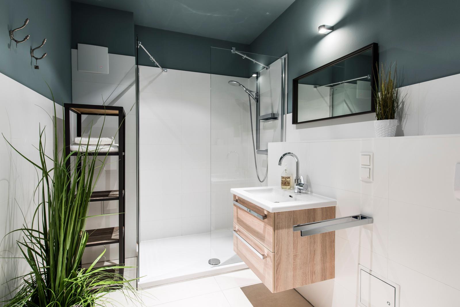 Badezimmer mit Dusche, Waschbecken und Pflanzen. Wandfarbe dunkelgrau, weiße Fliesen.