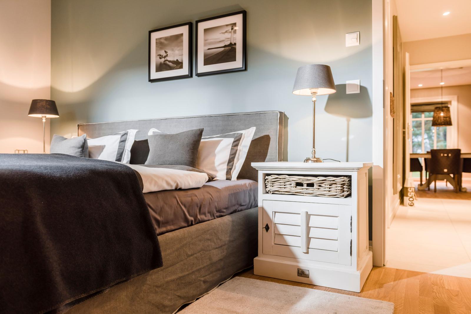 Schlafzimmer mit Bett, Nachttisch und Wandbildern. Durchgang in Wohnbereich.