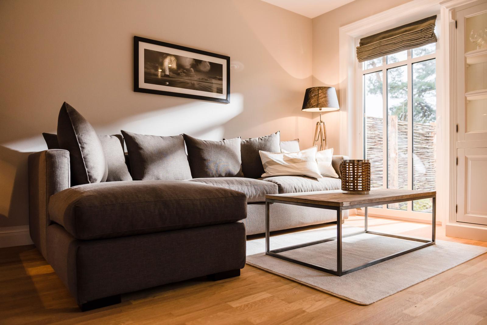 Ein Wohnzimmer mit grauem Sofa, Holztisch und Fensterblick auf Außenbereich.