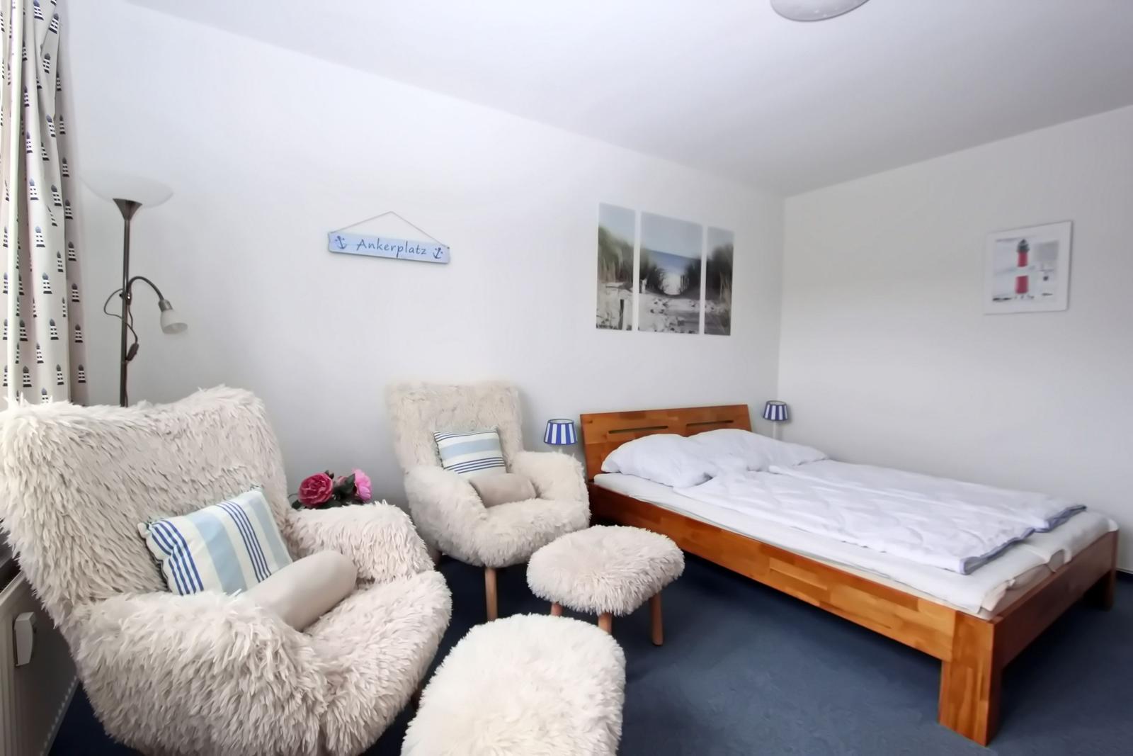 Schlafzimmer mit Bett, zwei Sessel und Wandbildern.