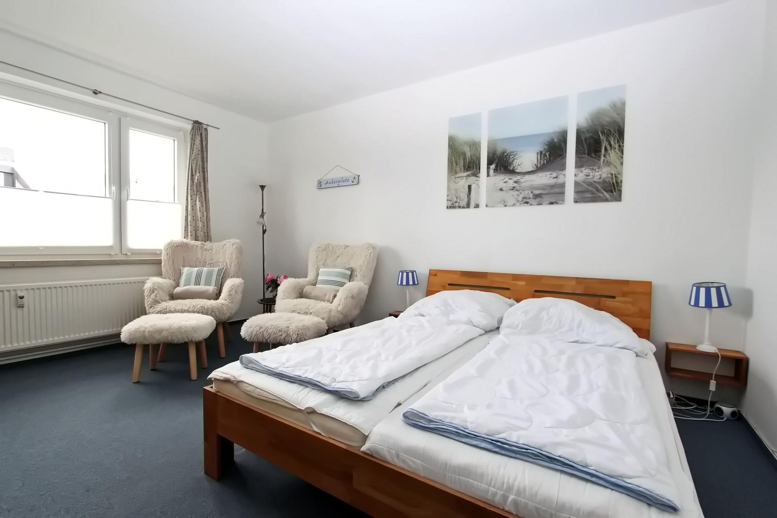 Ein Schlafzimmer mit Doppelbett, zwei Sesseln und Wandbildern.