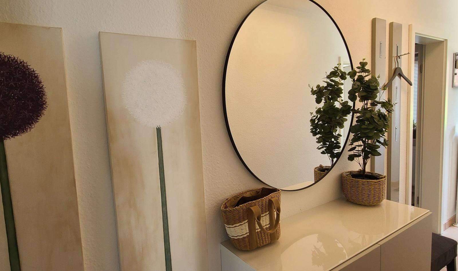 Schminktisch mit runden Spiegel, Pflanze und Körben an der Wand.