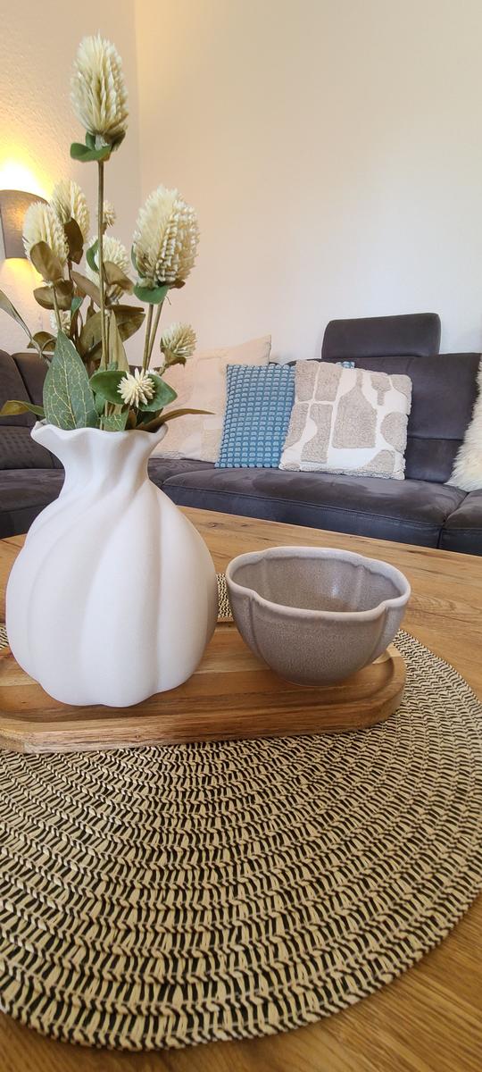 Ein Tisch mit Vasen und einer Schale auf einem runden Teppich vor einem Sofa.