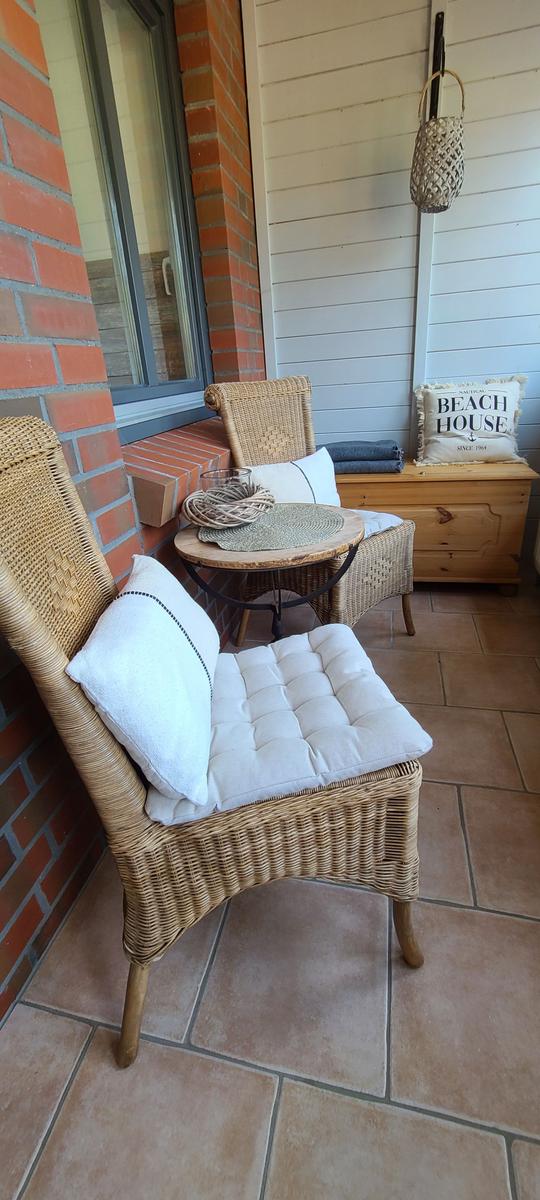 Terrasse mit zwei Rattanstühlen, Tisch und Kissen. Holzschrank mit Kissen daneben.