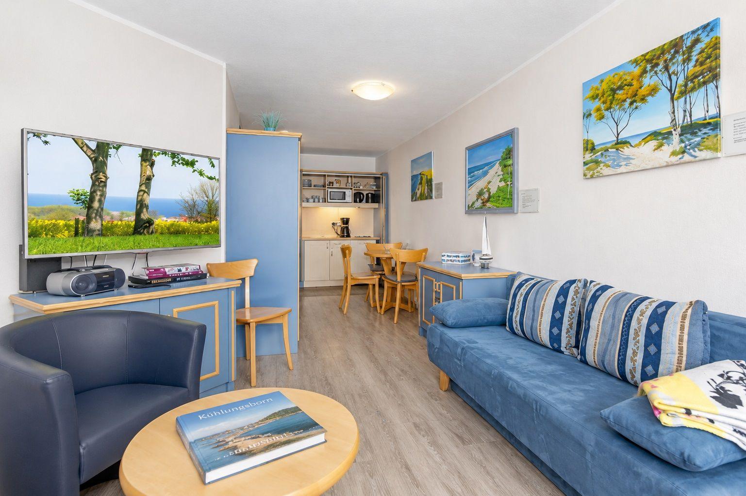 Wohnbereich mit Sofa, Fernseher und Essbereich. Wandbilder zeigen Strandlandschaften.