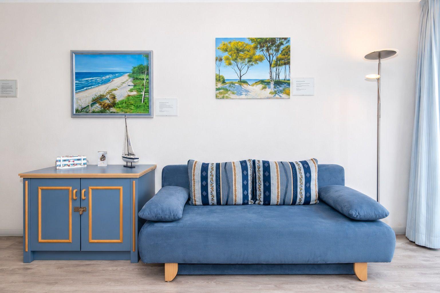 Blauer Sofa mit Kissen, blauer Schrank und Wandbilder mit Strandmotiven.