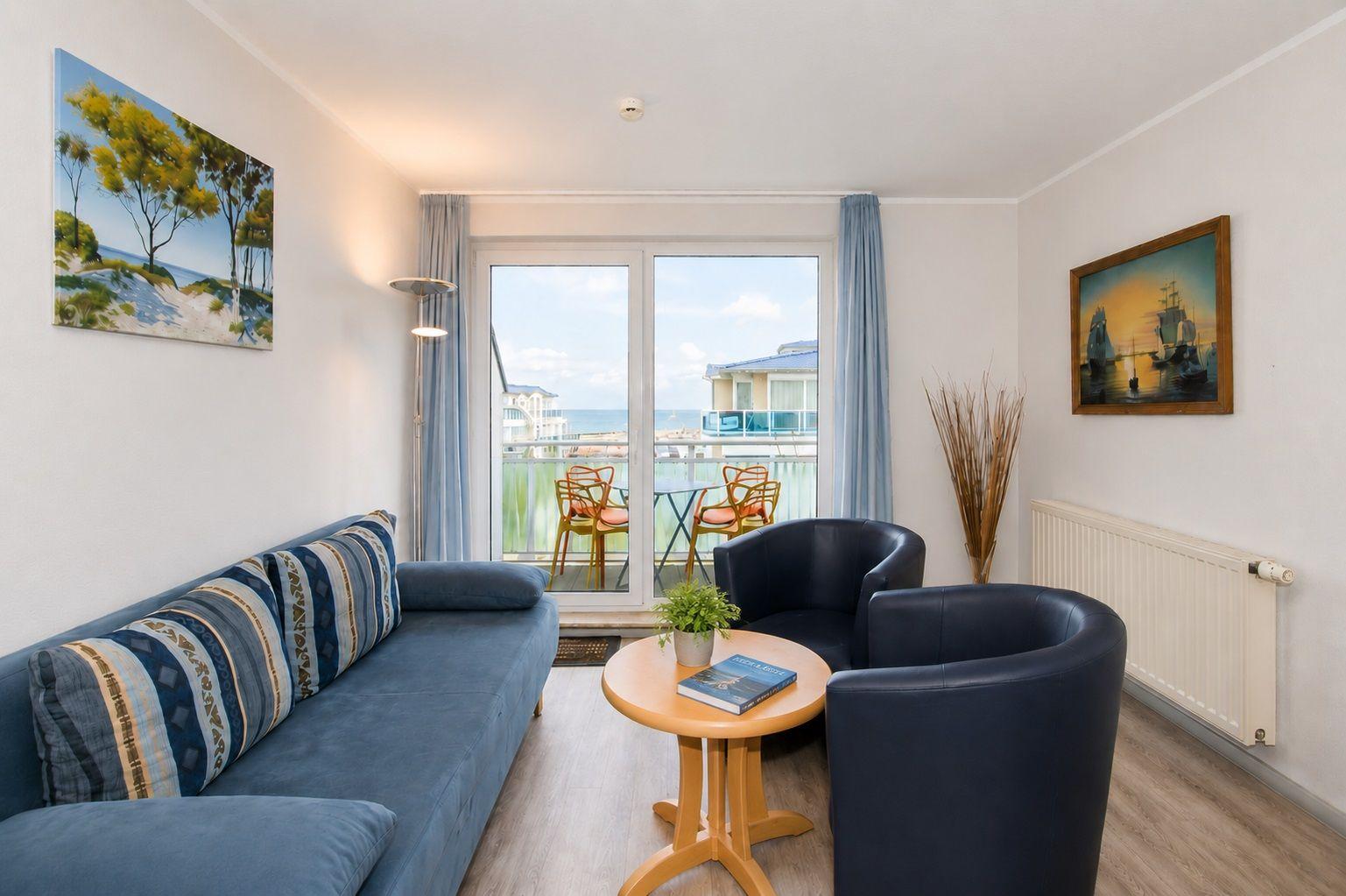 Wohnzimmer mit Sofa, zwei Sesseln und Balkonblick aufs Meer.