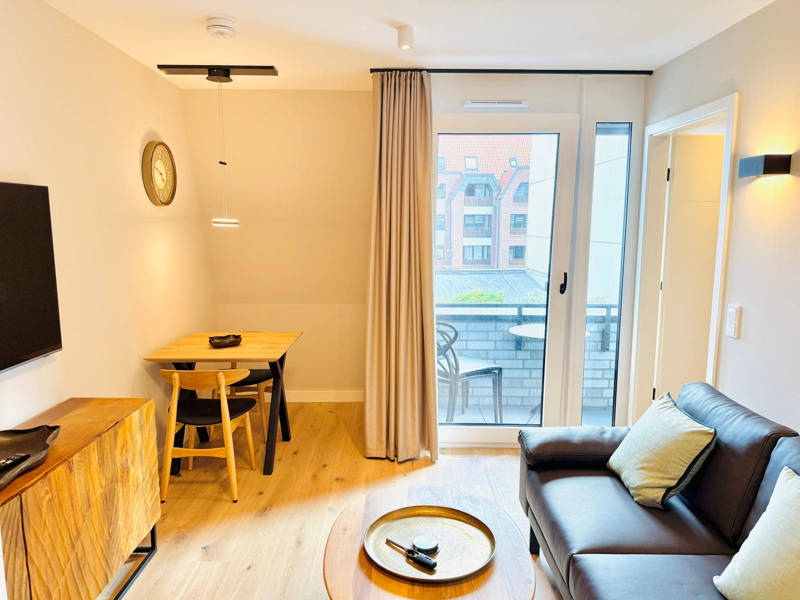 Wohnzimmer mit Sofa, Esstisch und Balkonzugang.