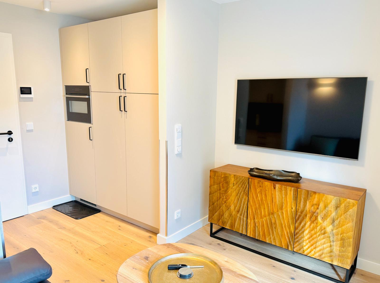 Küche mit eingebautem Ofen und Wohnbereich mit TV und Holzschrank.
