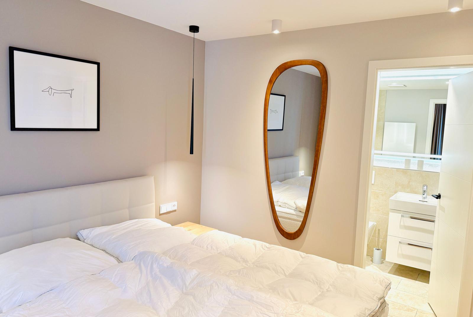 Schlafzimmer mit Doppelbett, Spiegel und angrenzendem Bad.