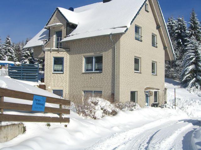 Ein zweistöckiges Haus mit Schneebedecktem Dach und Fenstern, umgeben von schneebedeckten Bäumen.