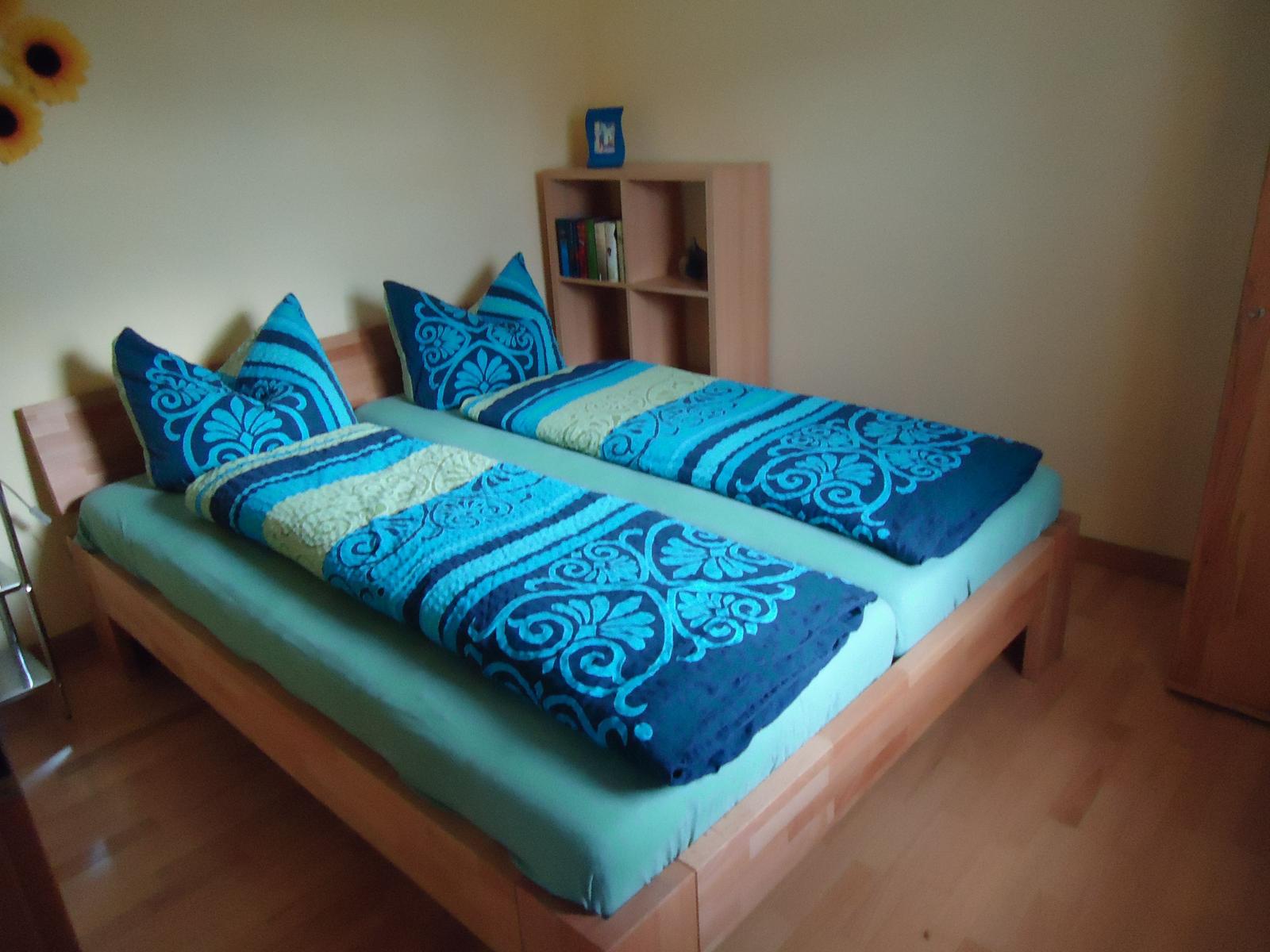 Ein Schlafzimmer mit einem Doppelbett, blau-weißem Bettzeug und einem Holzregal.