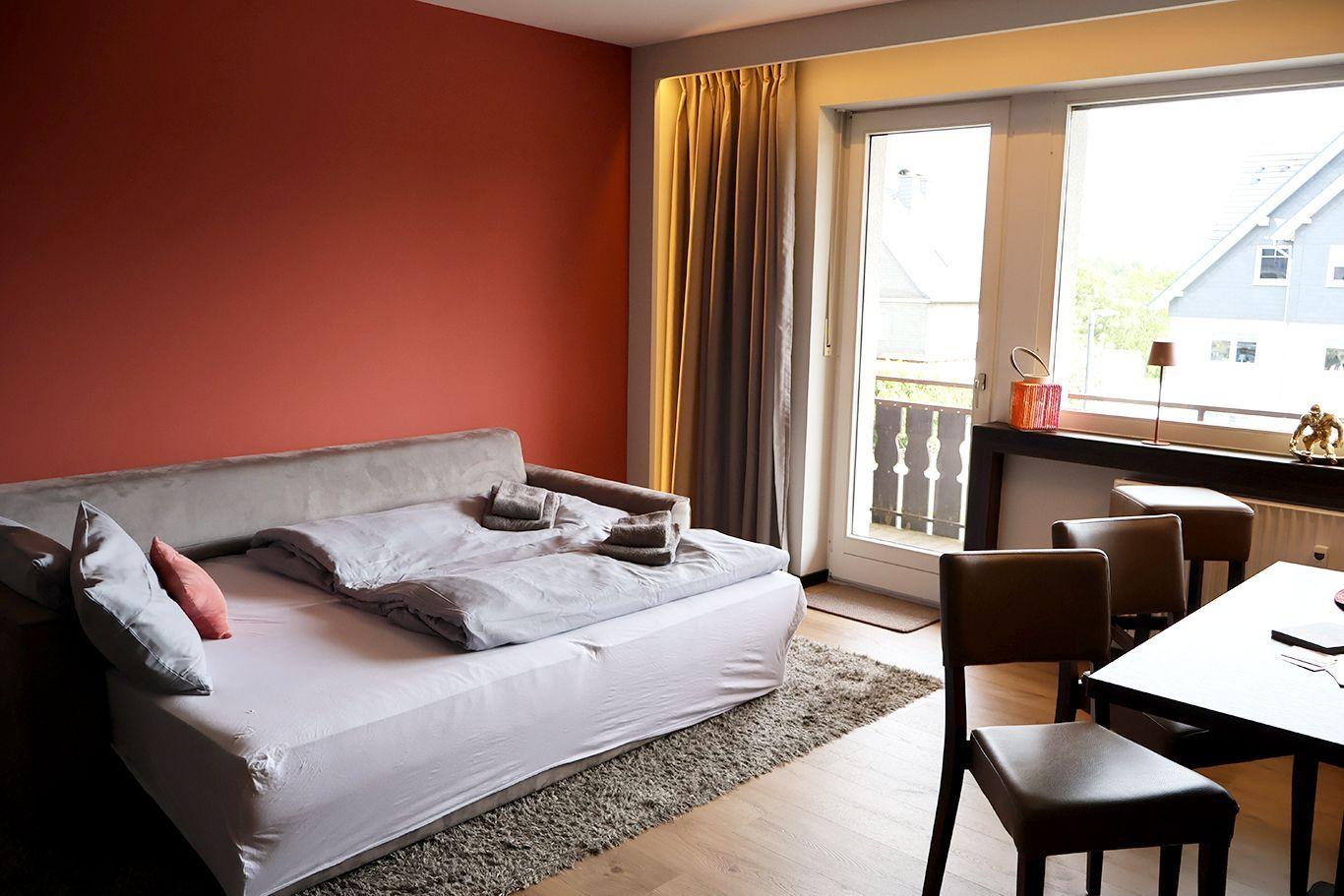 Schlafzimmer mit Bett, Tisch und Stühlen. Fenster mit Blick auf Balkon und Nachbarhaus.