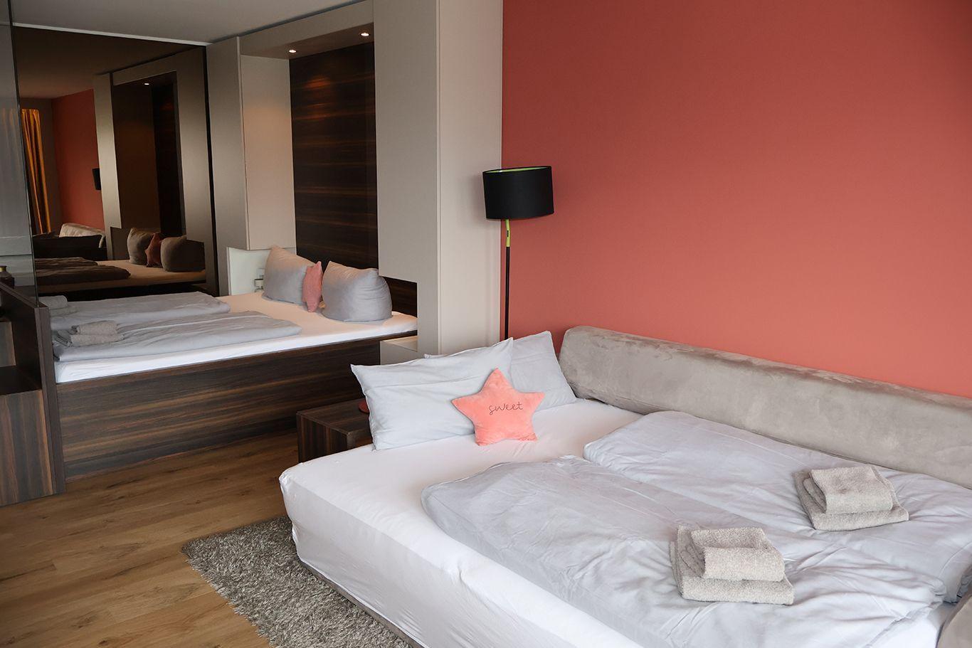 Schlafzimmer mit Doppelbett, rosa Wand und Spiegel. Handtuch auf Bett.