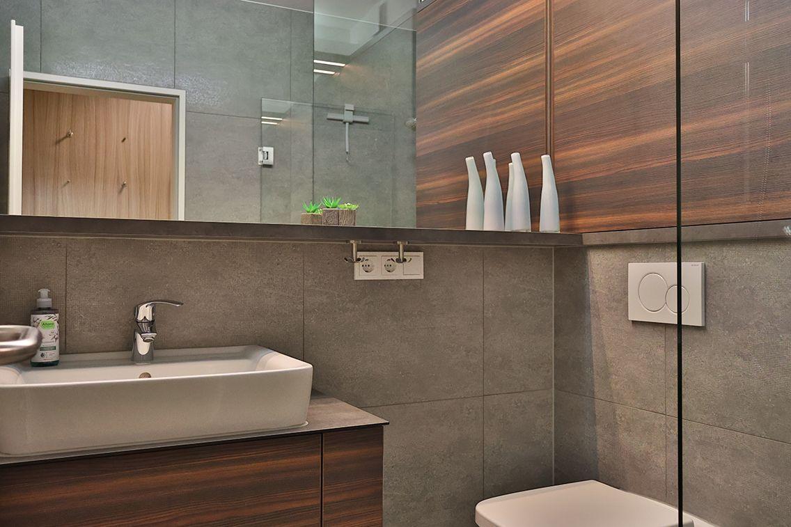 Bad mit Waschbecken, Spiegel und Holzschränken. Dusche mit Glaswand und Toilette.