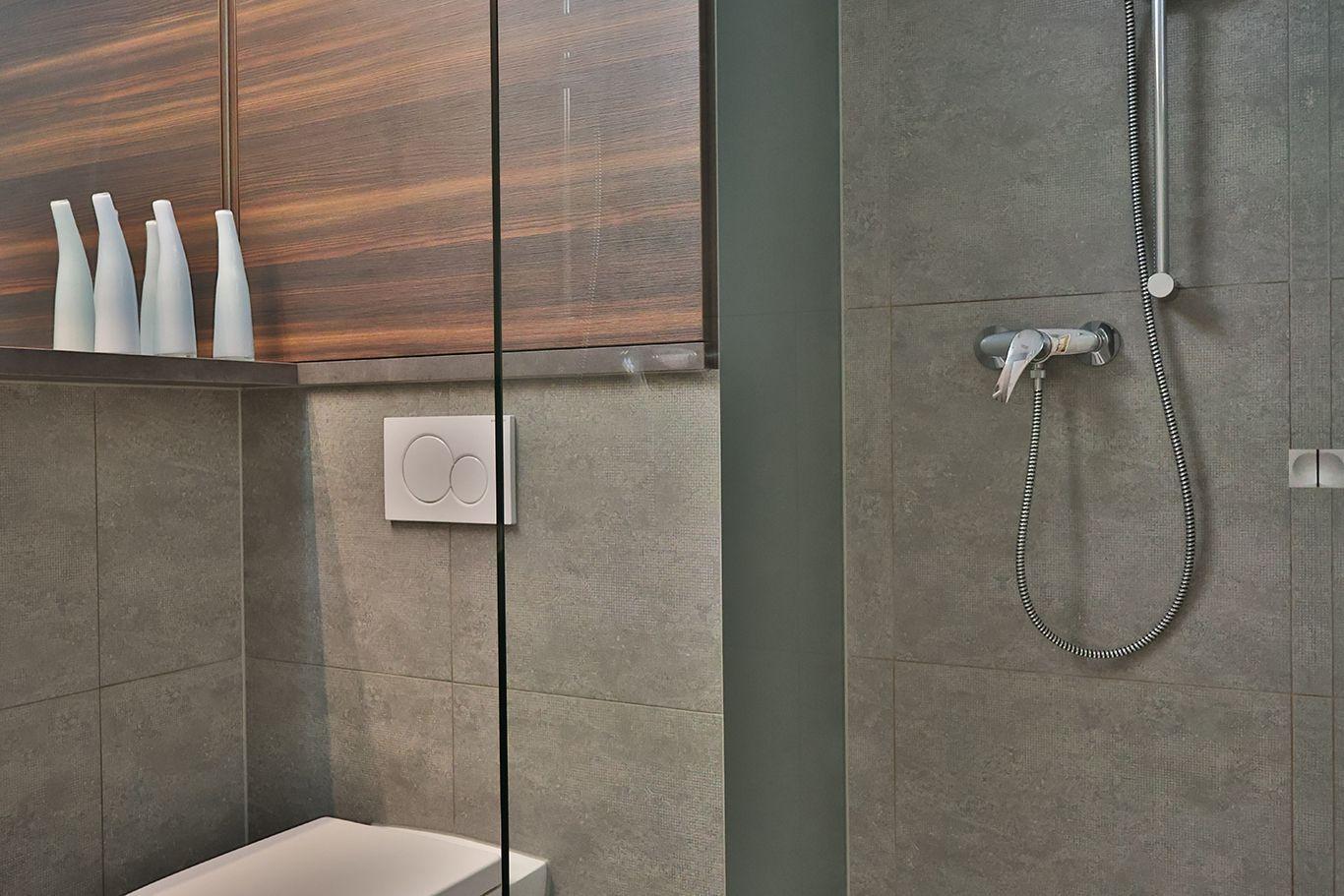 Bad mit Dusche, Toilette und Holzschränken. Graue Fliesen und weiße Keramik.
