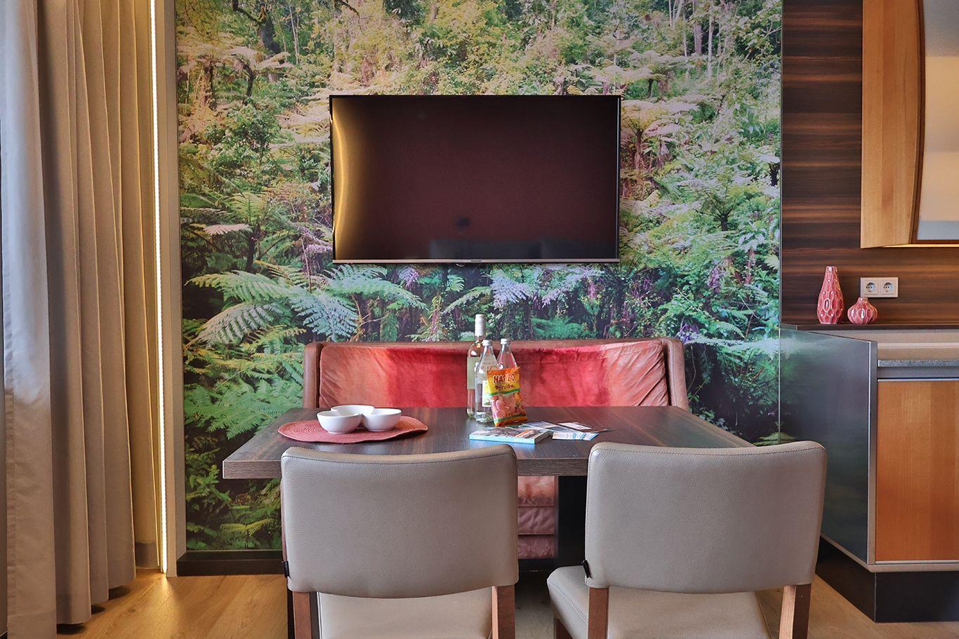 Essbereich mit Tisch, Stühlen und Fernseher an Waldtapete