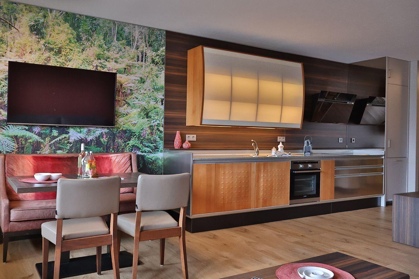 Küche mit Holzschränken, Essbereich und Wandbild mit Waldmotiv.