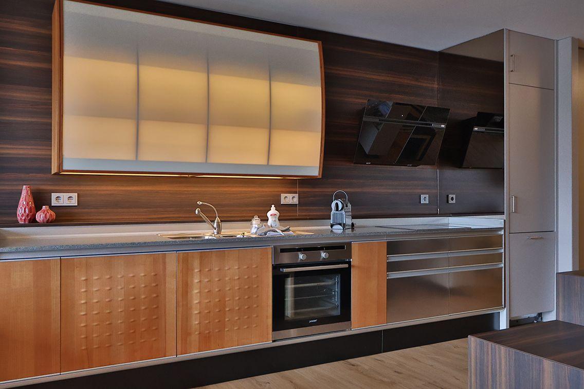 Moderne Küche mit Holzschränken, Edelstahlgeräten und beleuchtetem Oberlicht.