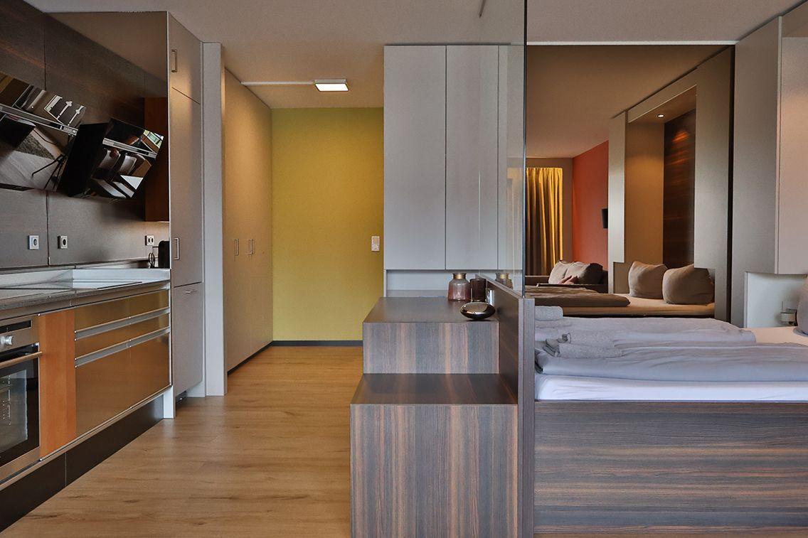 Moderne Wohnung mit Küchenbereich und Schlafzimmer. Holzboden und Glaswand sichtbar.