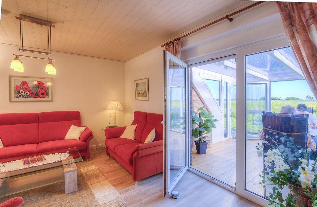 Wohnzimmer mit roten Sofas, Glas-Tisch und Blick auf Terrasse mit Garten.
