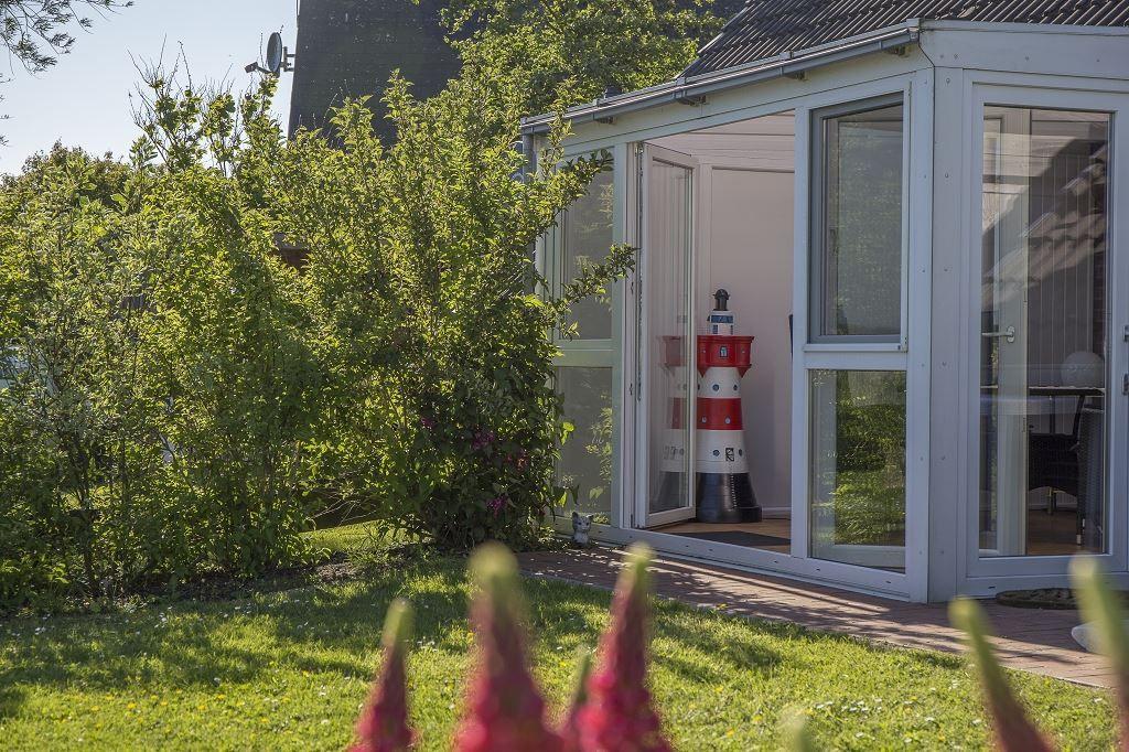 Garten mit Blick auf eine Glasveranda mit rotem Leuchtturmmodell.