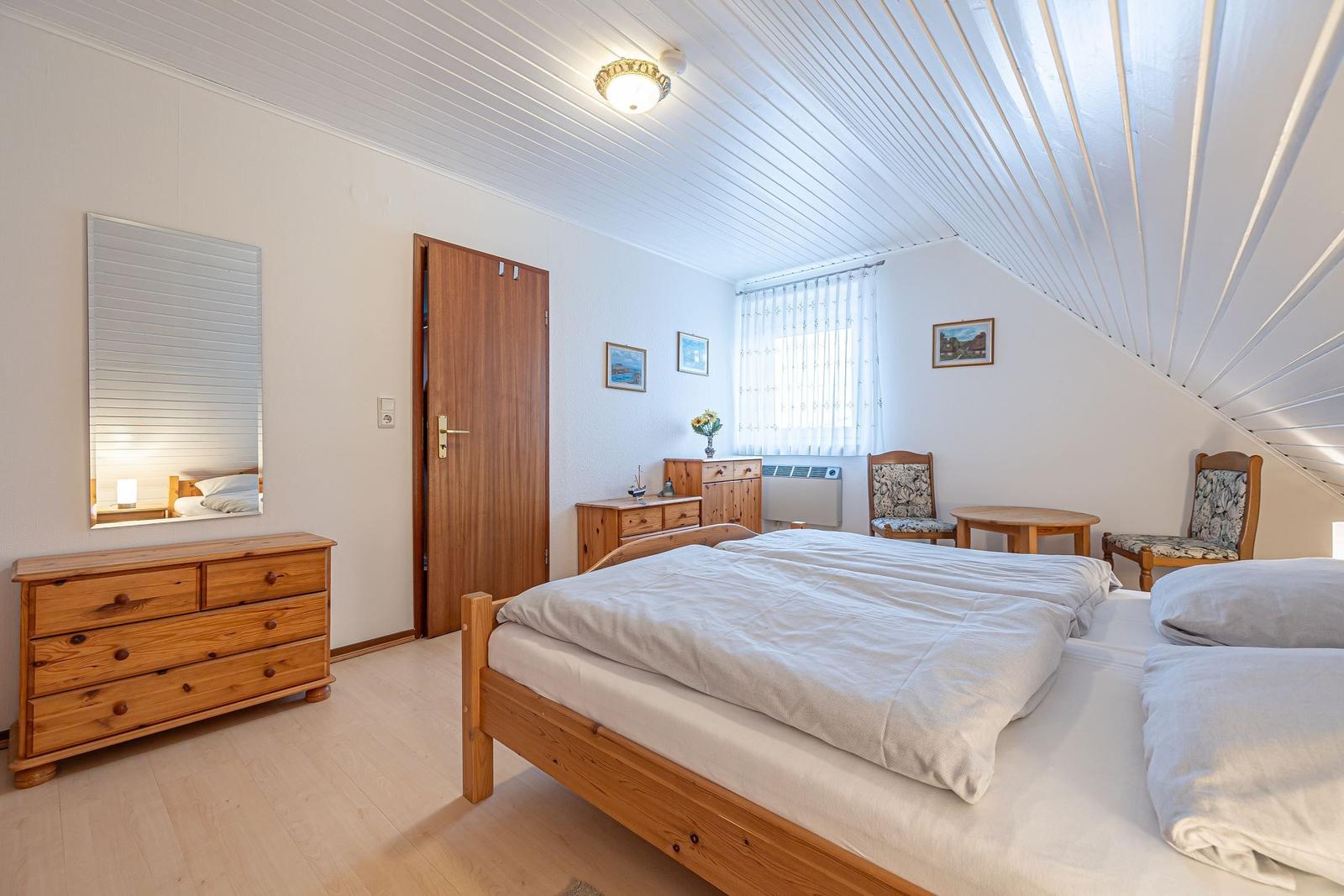 Schlafzimmer mit Holzbett, Kleiderschrank und Sitzgelegenheit unter Dachschrägen.