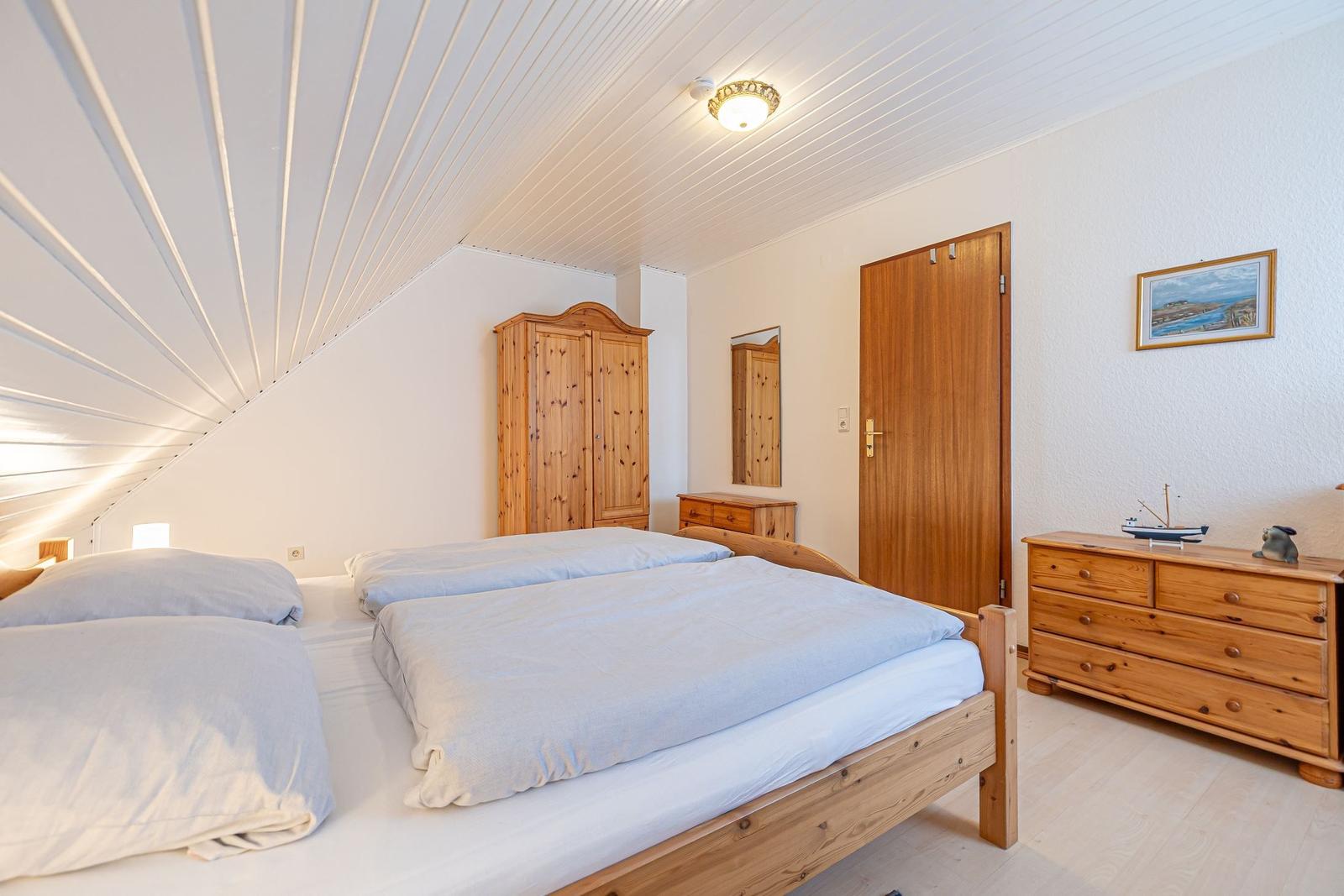 Schlafzimmer mit Doppelbett, Holzmöbel und schrägem Dach