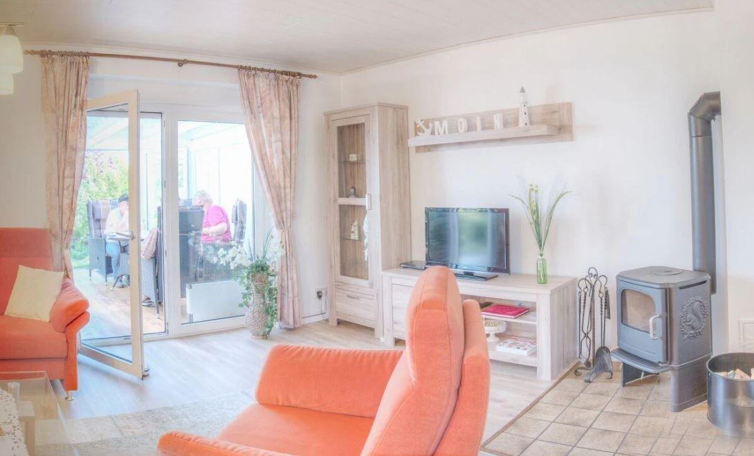 Wohnzimmer mit orangefarbenen Sesseln, Kaminofen und Glasfront zur Terrasse.