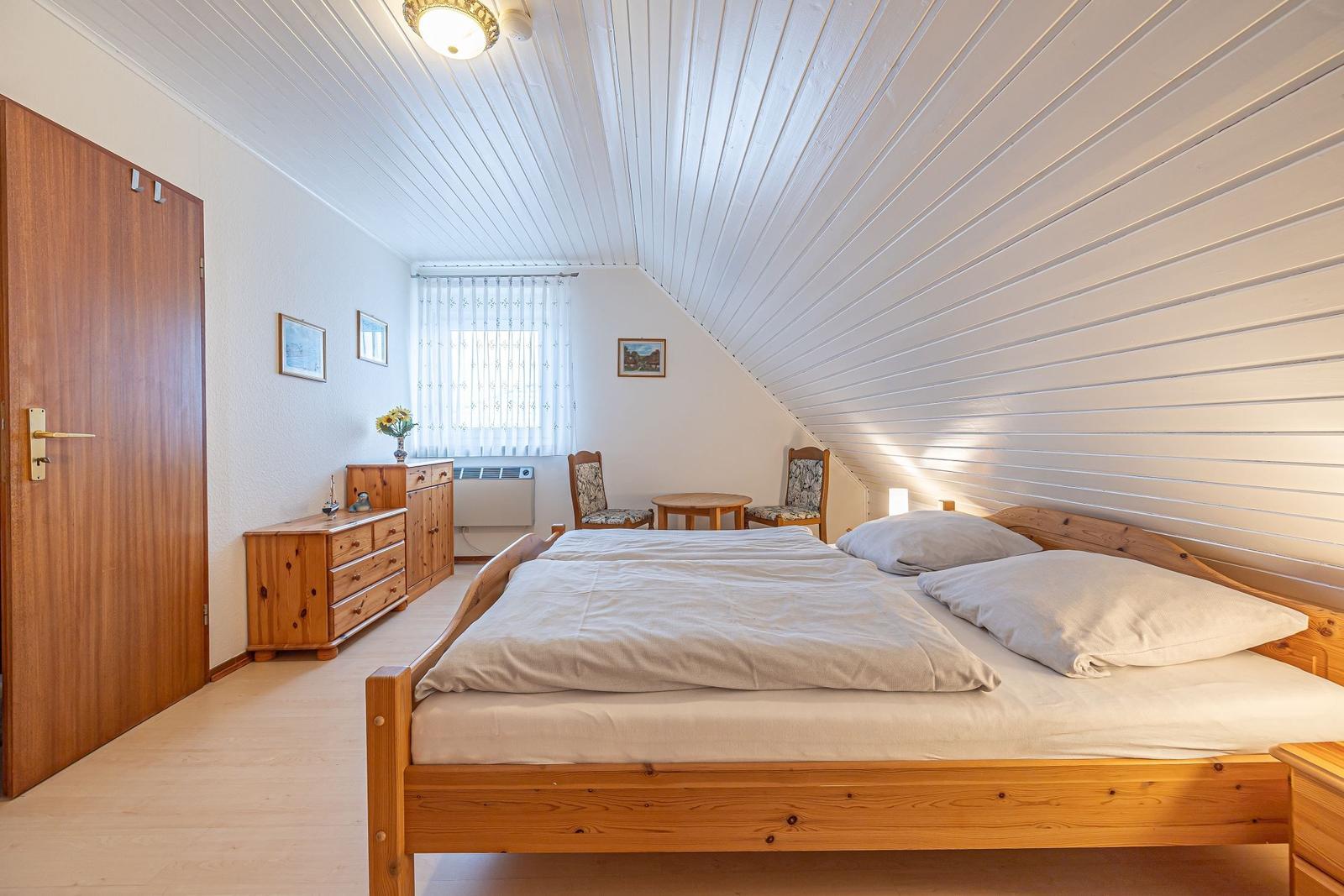 Schlafzimmer mit Holzbett, Schrank und Tisch. Dachboden mit weißer Holzdecke.