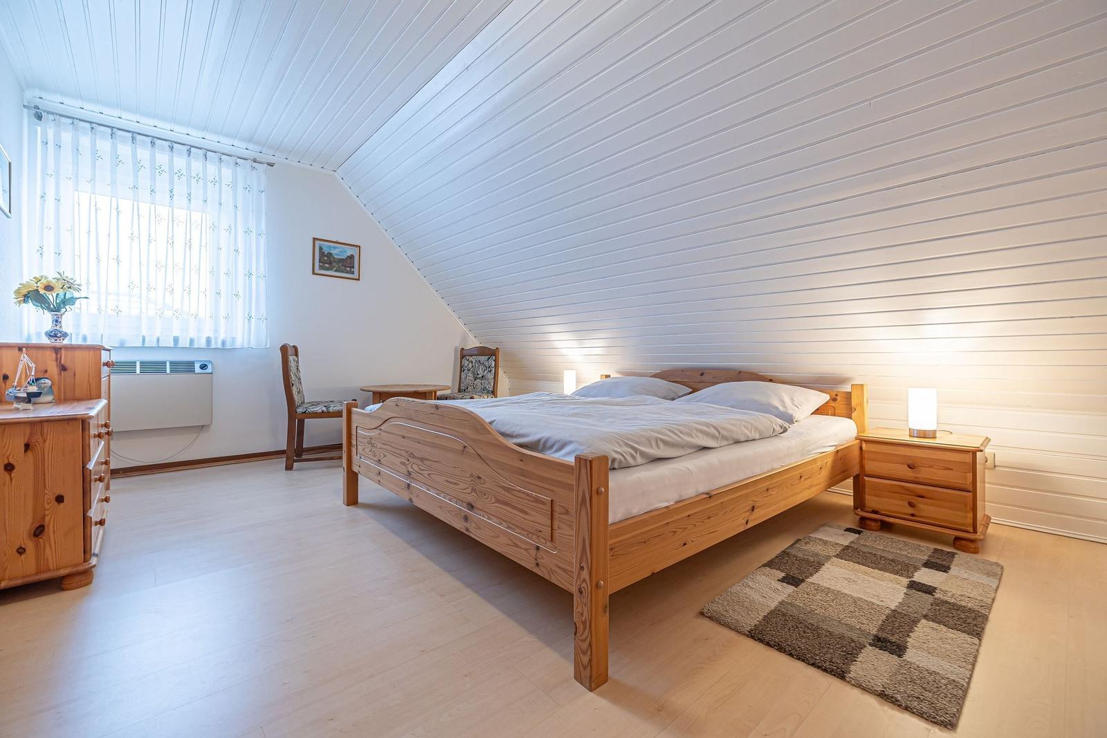 Schlafzimmer mit Holzbett, Nachttisch und Fenster mit Vorhang.