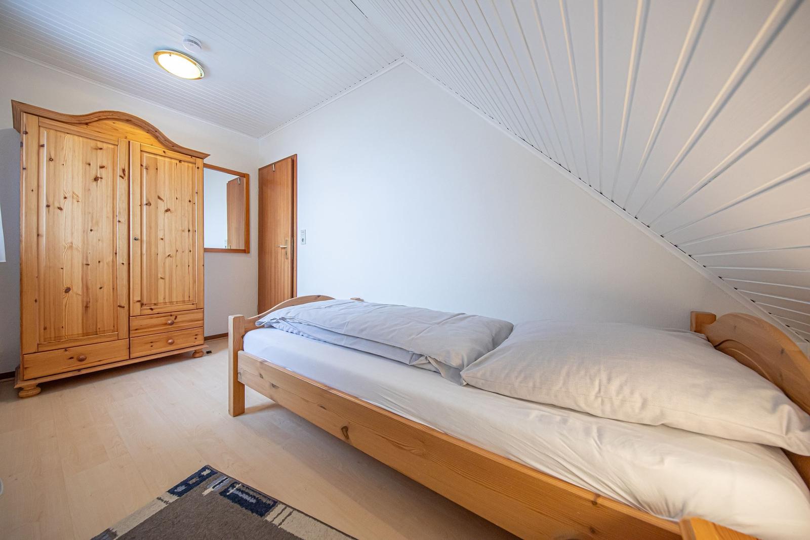 Schlafzimmer mit Holzbett, Kleiderschrank und schräger Decke.