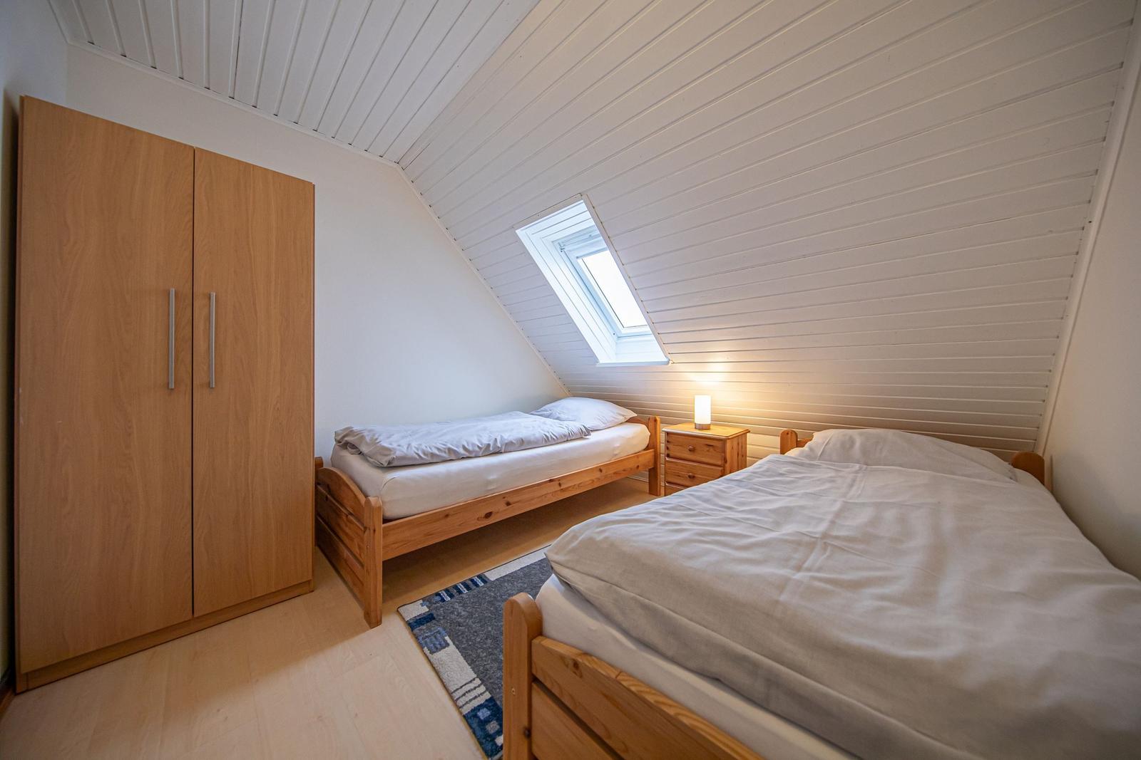 Zimmer mit zwei Betten, Schrank und Dachfenster. Holzboden und weiße Wände.