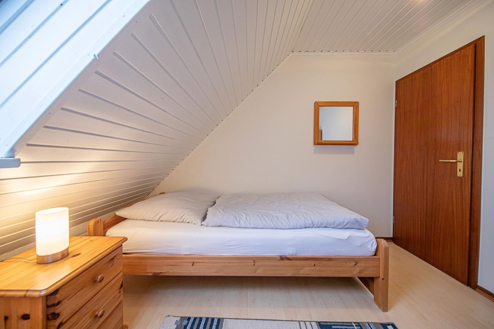 Schlafzimmer mit Holzbett, Nachttisch und Spiegel an der Wand