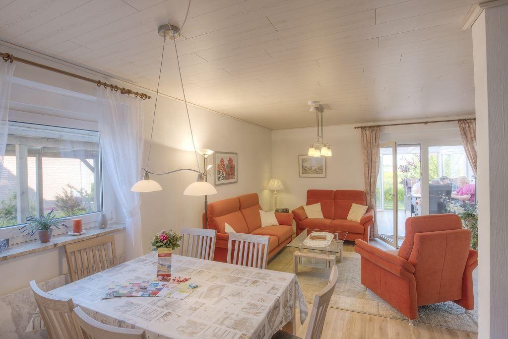 Wohn- und Essbereich mit orangefarbenen Sofas, Tisch und Stühlen sowie Fenstern und Glastür.