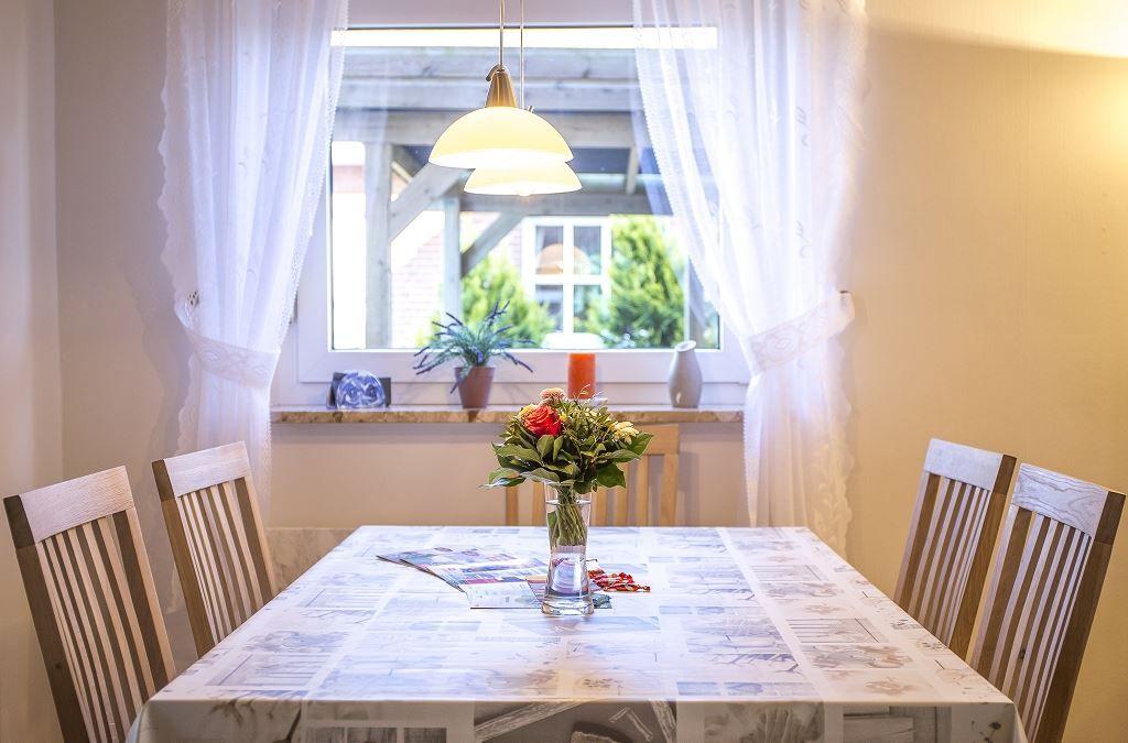 Esstisch mit Stühlen, Blumen und Fenster mit Vorhängen.