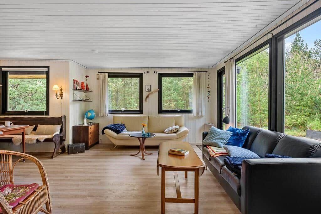 Wohnzimmer mit Sofa, Couch und Tischen. Große Fenster mit Blick auf Wald.