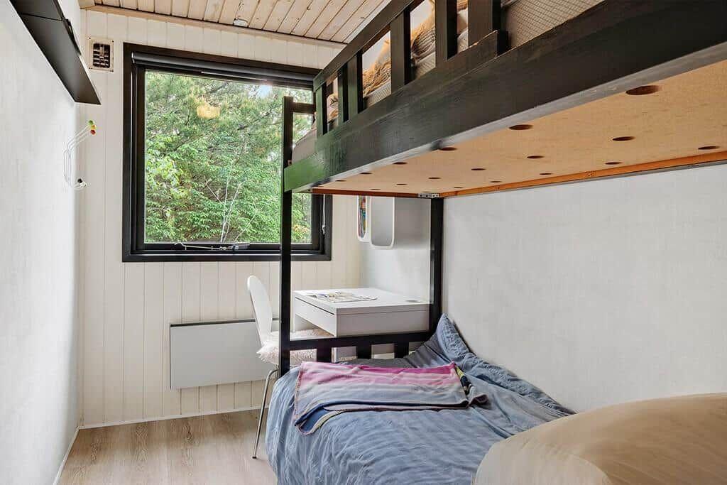 Schlafzimmer mit Doppelstockbett, Schreibtisch und Fenster zum Wald.