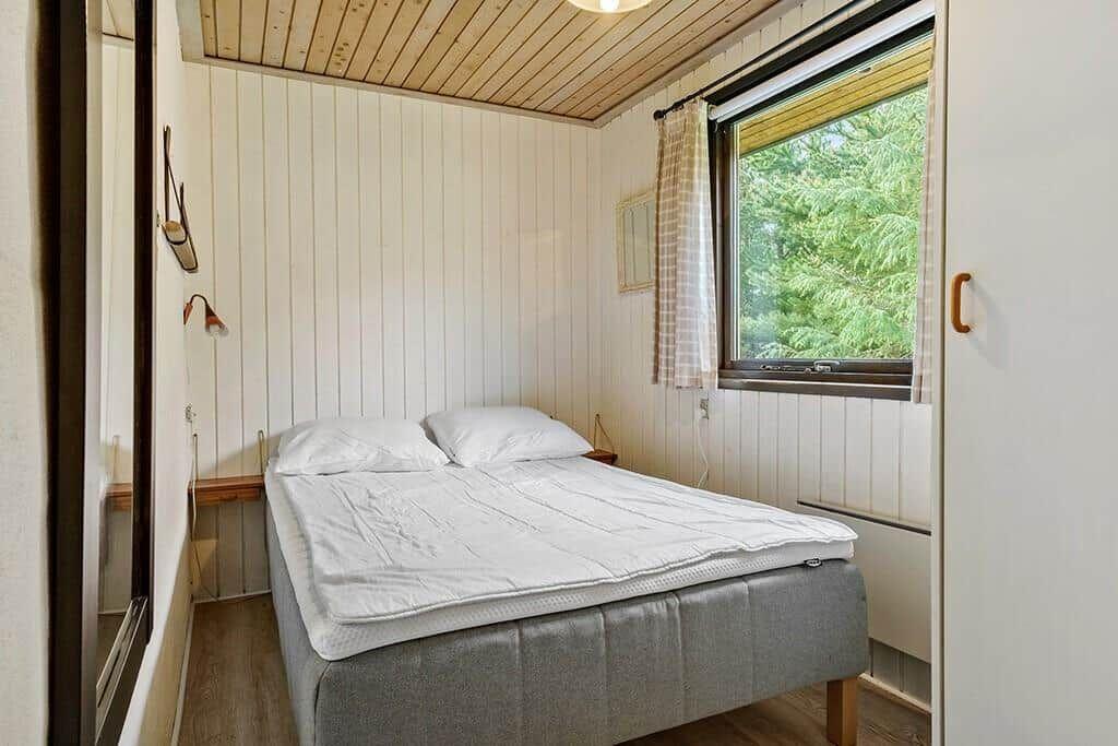 Schlafzimmer mit Bett, Fenster und Holzdecke.