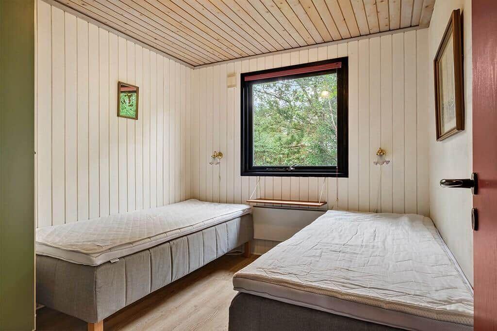 Zwei Betten in einem Raum mit Holzdecke und Fenster zum Wald.