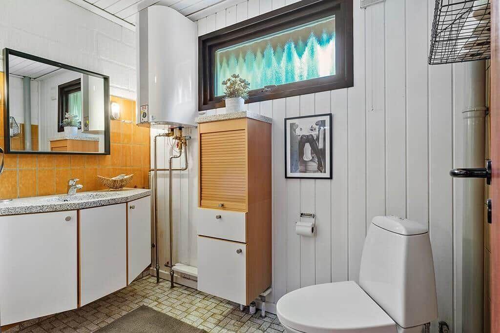 Badezimmer mit Waschbecken, Spiegel, Toilette und Holzschränken.