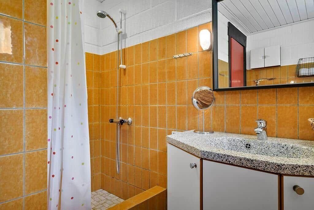 Badezimmer mit Dusche, Waschbecken und Spiegel an orangefarbenen Fliesen.